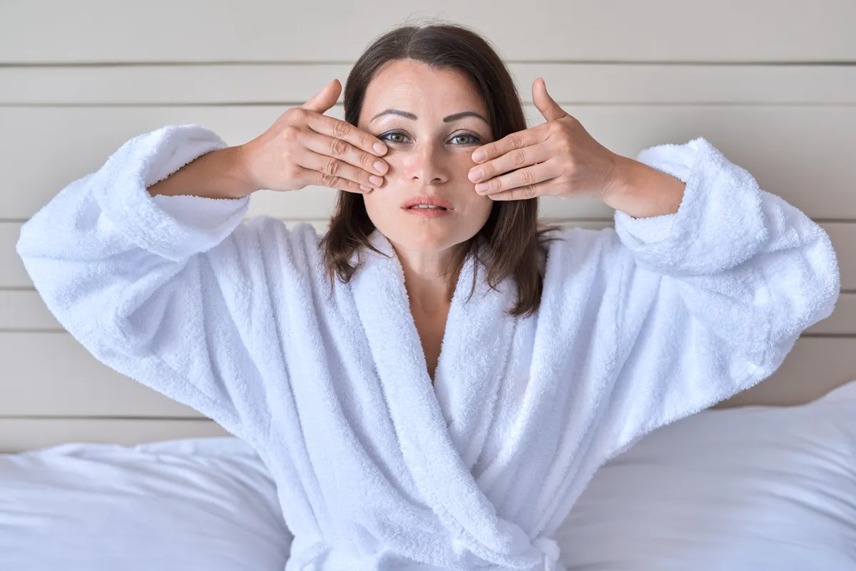 Otthoni arcmasszázst alkalmazó középkorú nő.