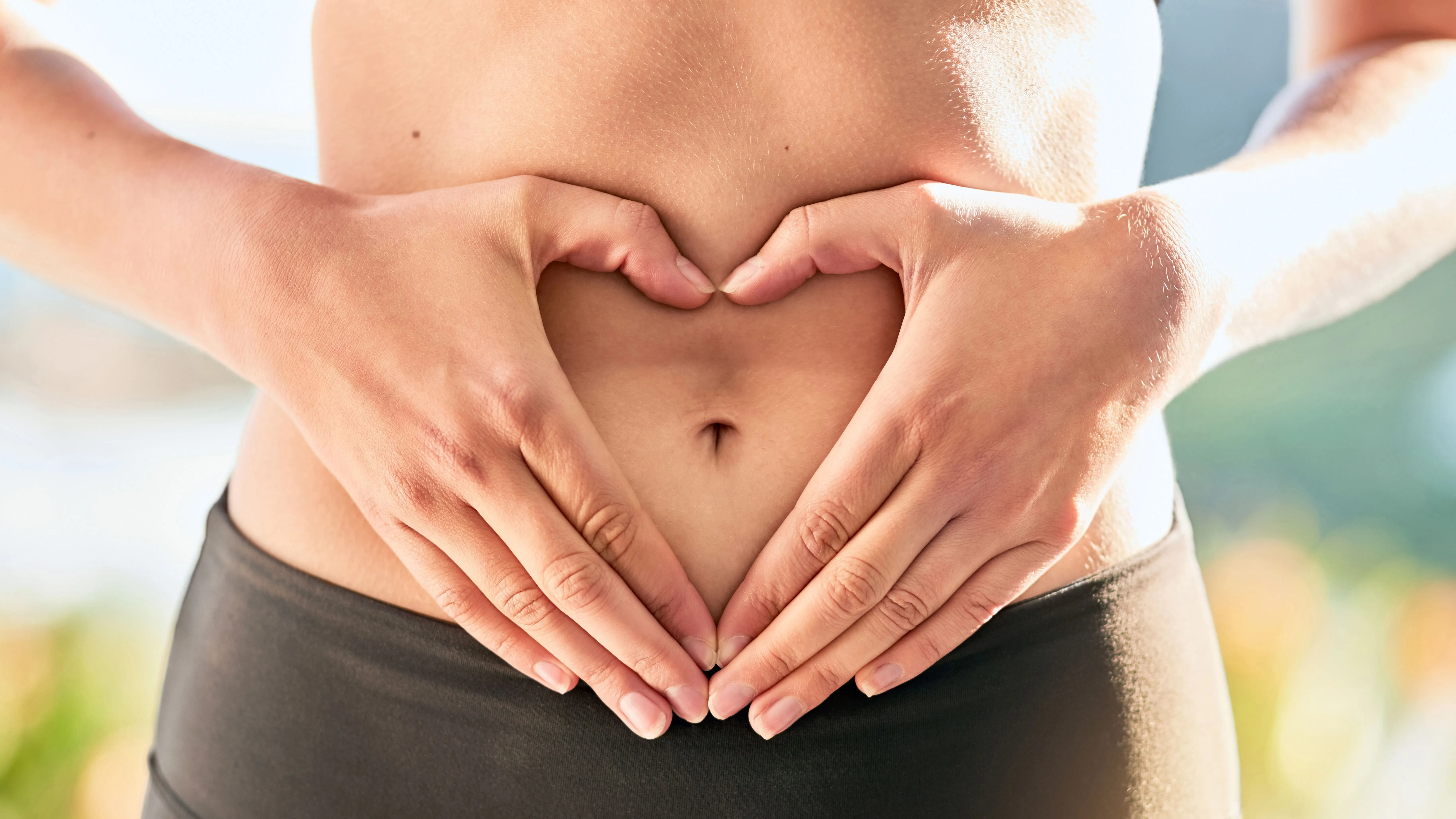 A meztelen hasa előtt a kezeivel szív alakot formáló nő, aki a fibre layering módszerét alkalmazza