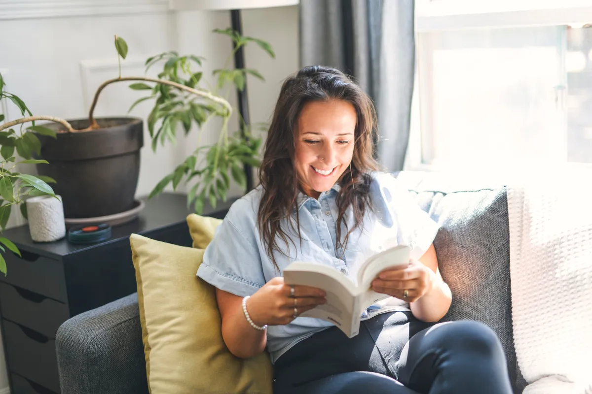Kanapén olvasó boldog nő a műveltségi kvízben.