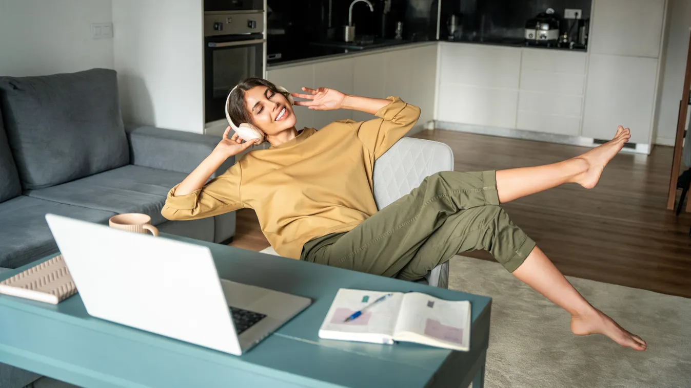 Személyiségtesztben szereplő kép egy boldog, fiatal, laptop előtt boldogan zenét hallgató nőről