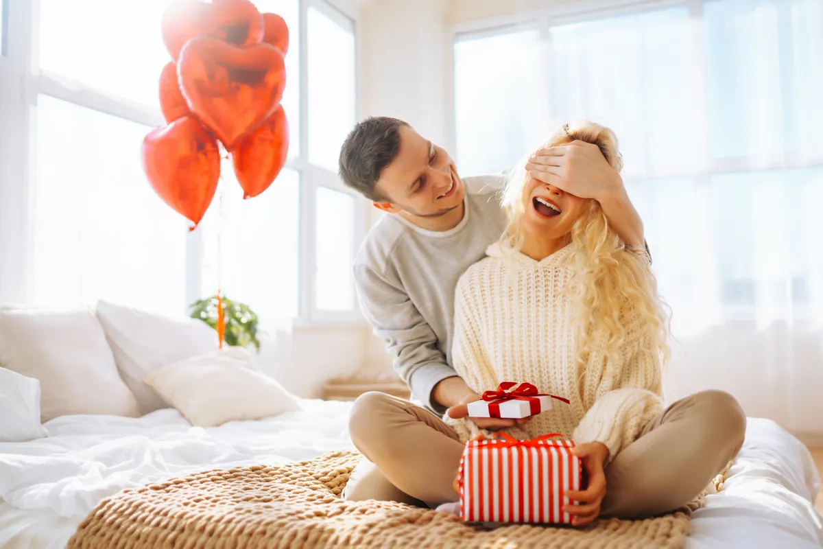 Ágyon ülő szerelmespár Valentin-napi meglepetéssel.