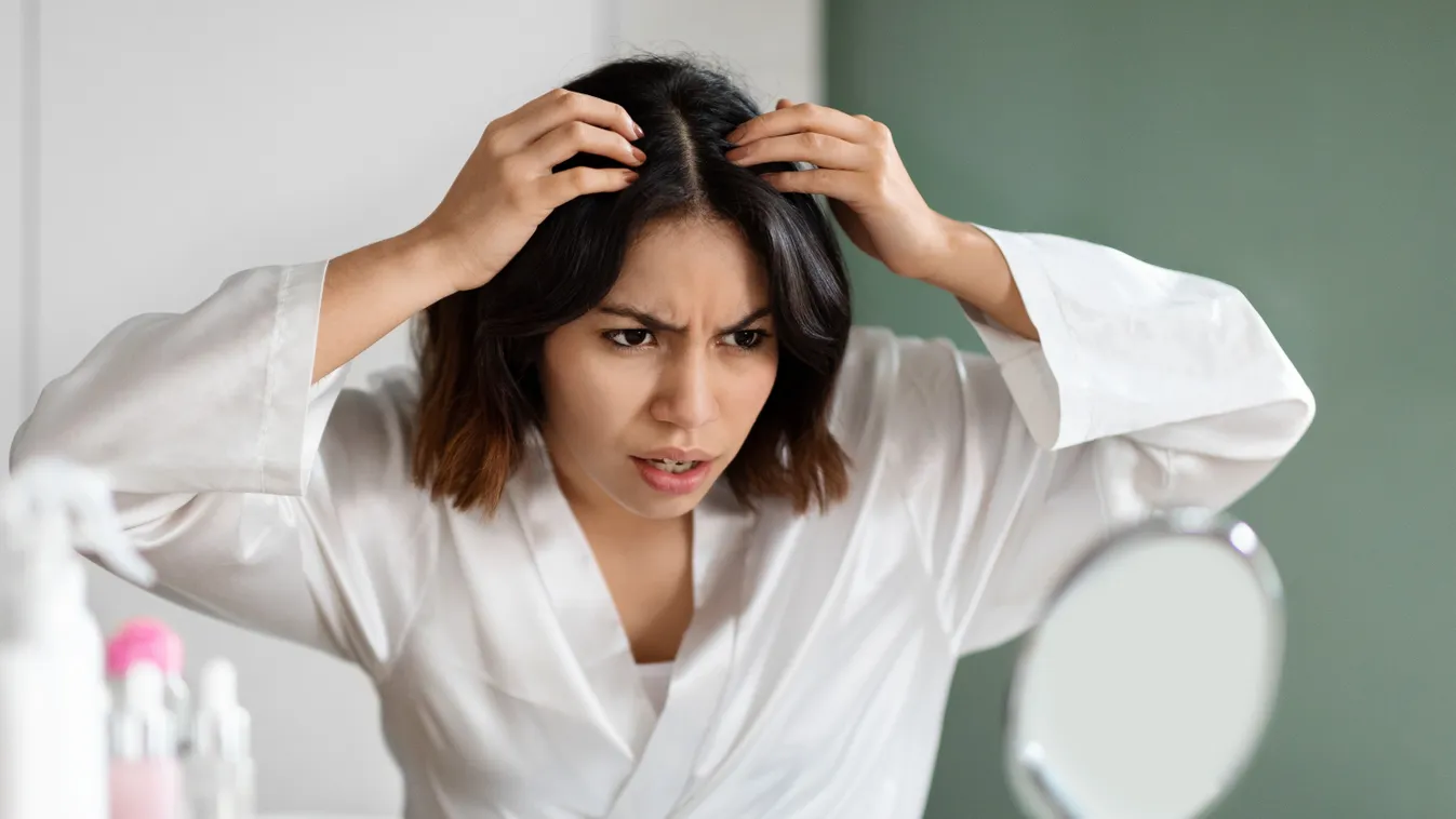 Ideges nő, aki észrevett egy ősz hajszálat a tükörben.