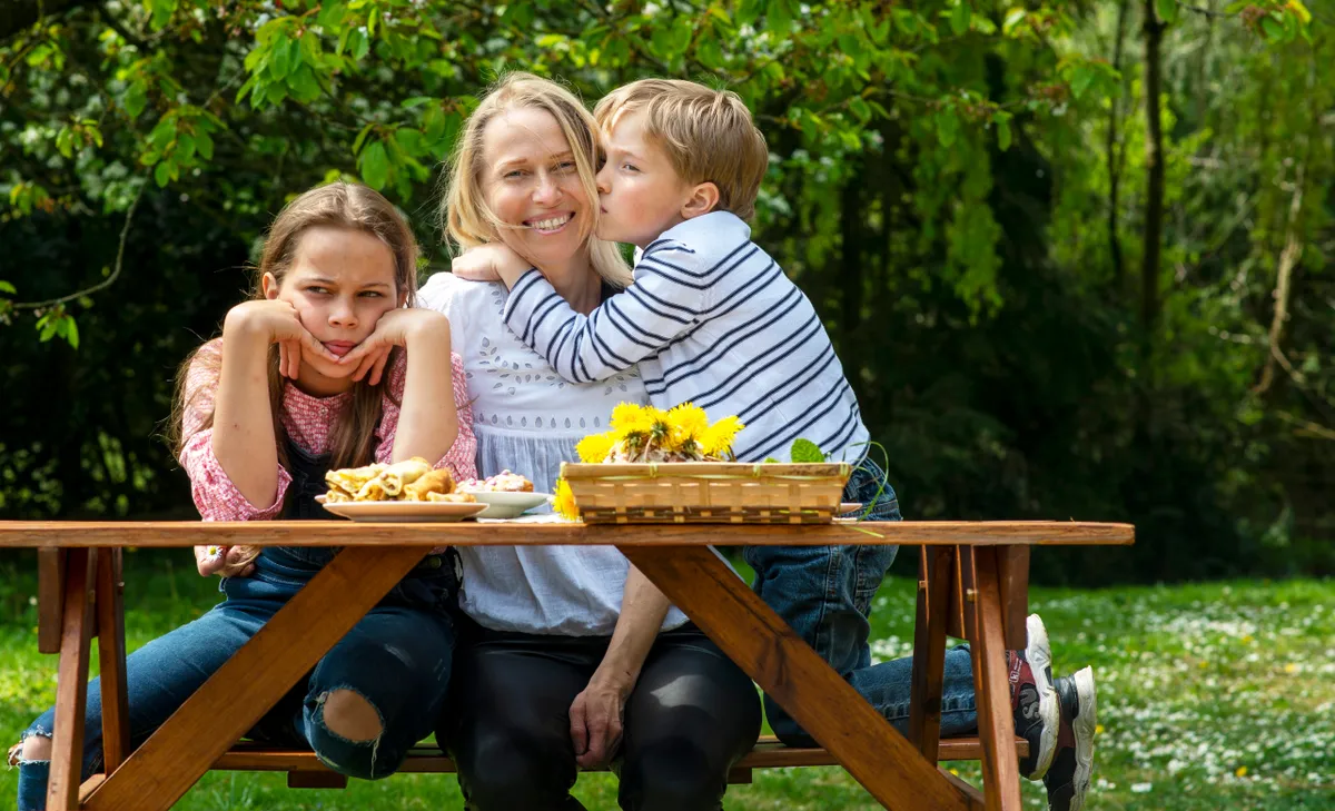 Az anyuka kedvenc gyereke ül az ölében, bal oldalán a lánya egy padon.