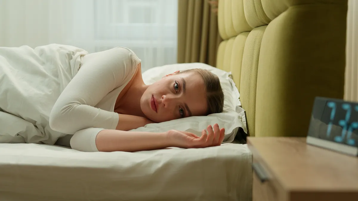 Ágyban fekvő álmos nő egy reggeli hiba elkövetése közben