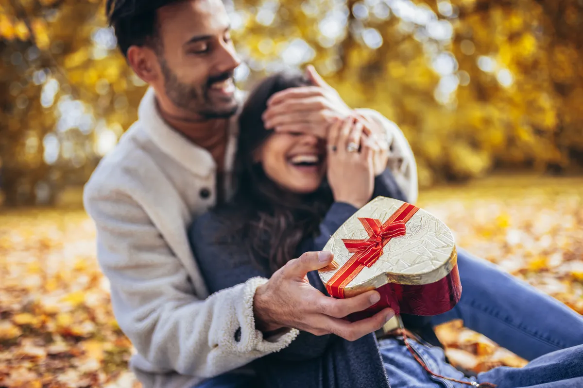 Valentin-napi ajándékot adó férfi öleli a mosolygó párját.