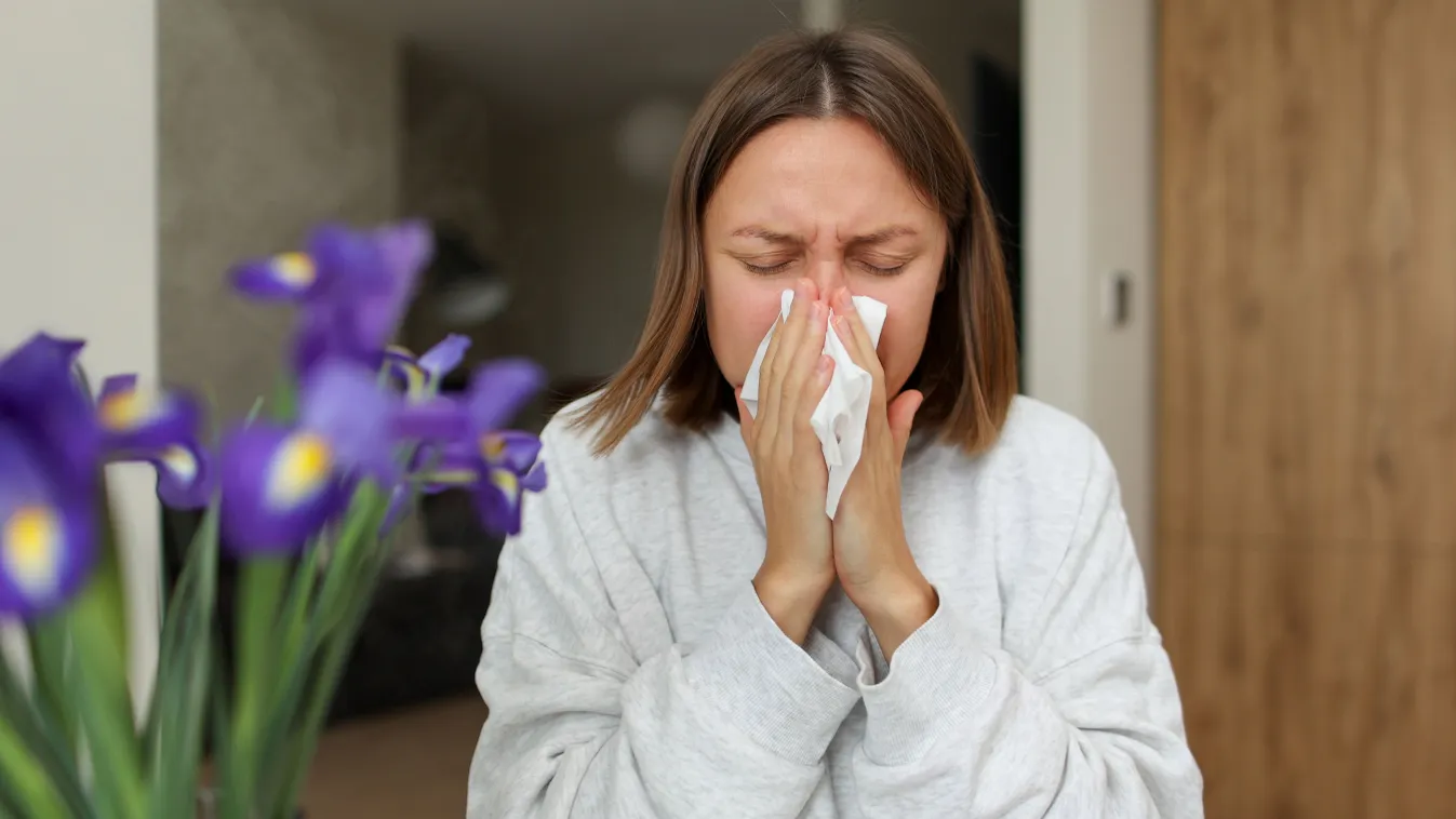 Az allergia töneteit tapasztaló nő fújja az orrát.