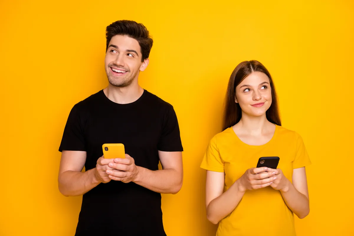 Párkapcsolatban lévő fiatal pár egymás mellett telefonozva