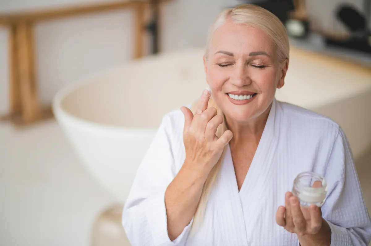 Középkorú nő menopauza alatt, aki krémezi az arcát.