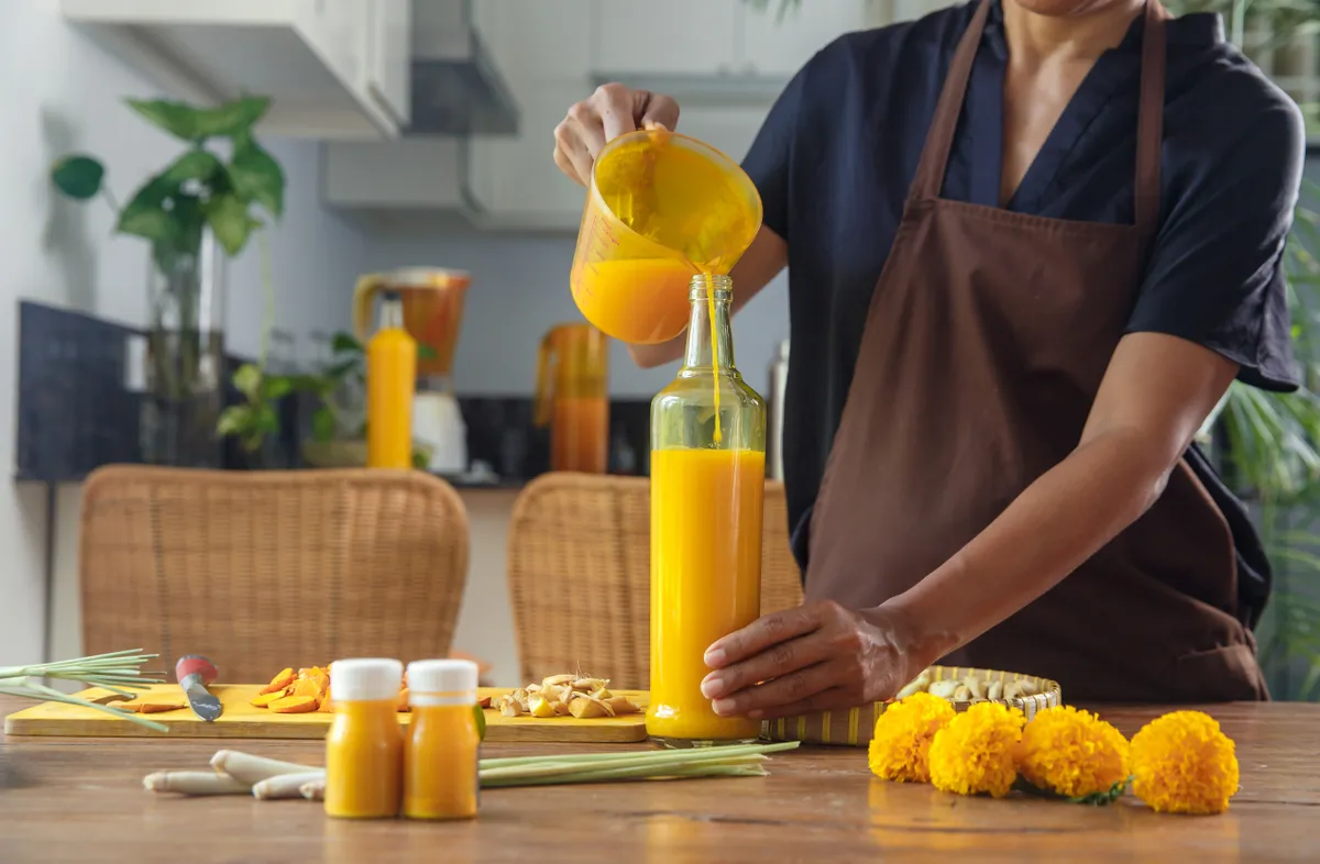 Gyömbérből és gyümölcsökből készült italt üvegbe kitöltő nő