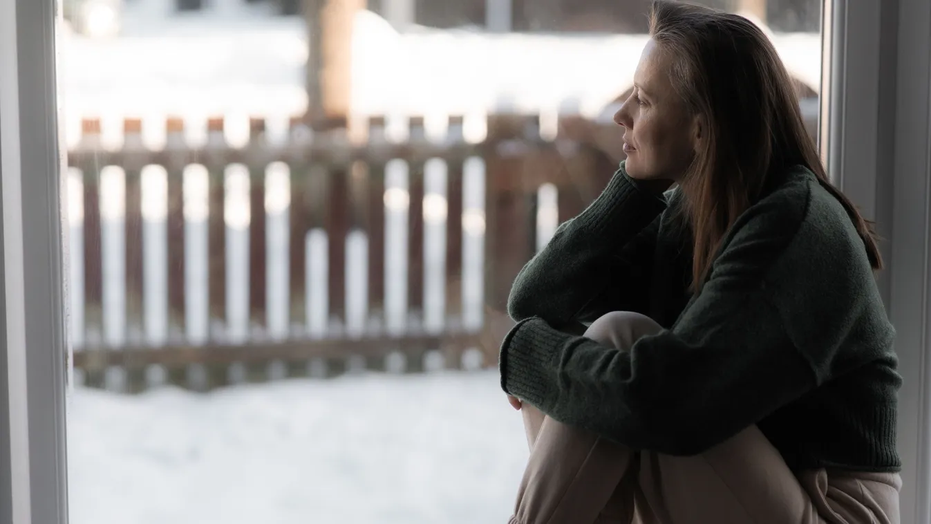 Téli depressziótól szenvedő nő ül az ablakban. 