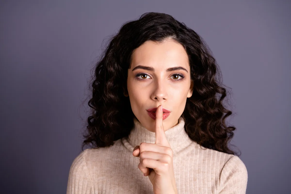 Ujját a szája elé emelő fiatal nő, aki a horoszkóp szerint a megbízható csillagjegyek egyike