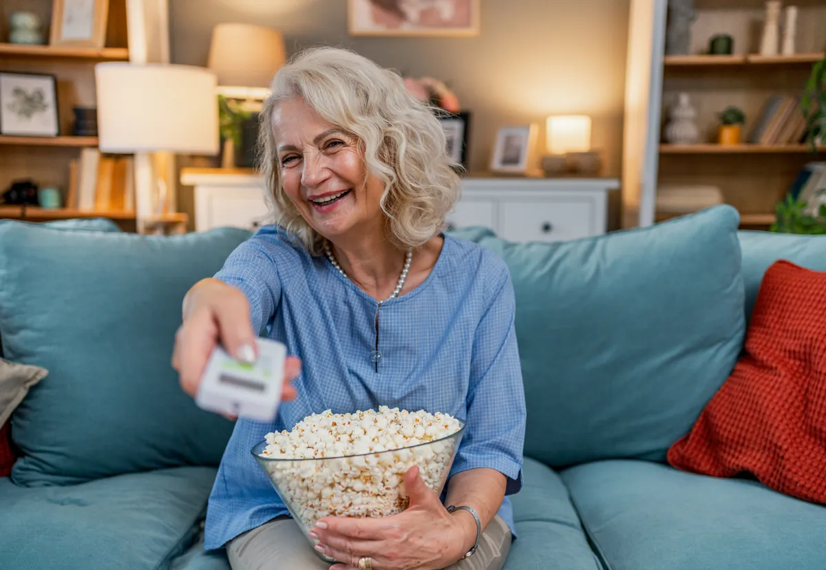 Idős nő esti nassolás közben a kanapén pattogatott kukoricát majszolva