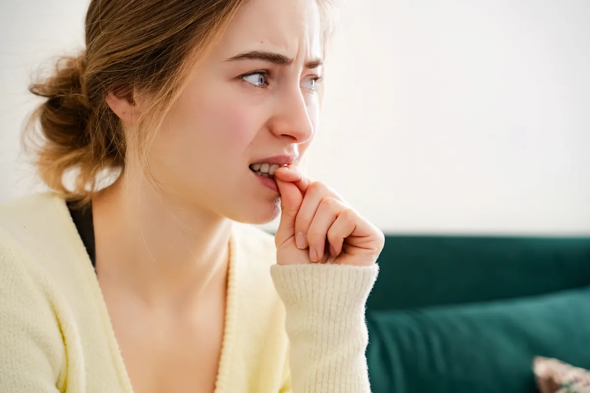 Rohanó nő szindrómában szenvedő fiatal, stresszes nő rágja a körmét.