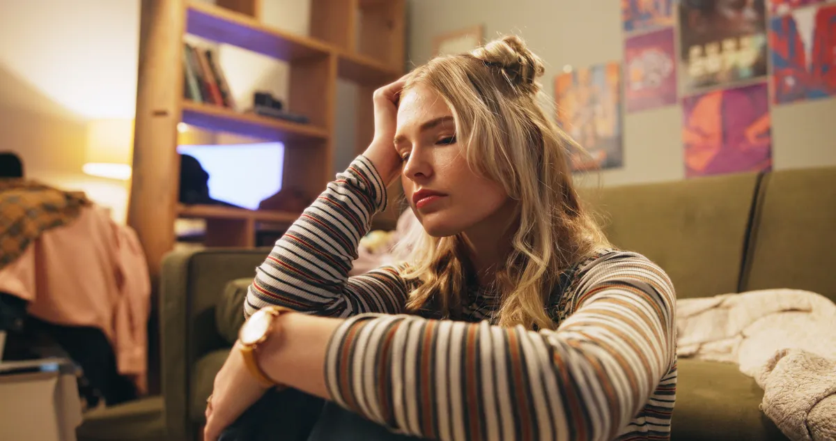 Folsavhiányban szenvedő fiatal nő fáradtan ül egy kanapé tövében a fejét fogva