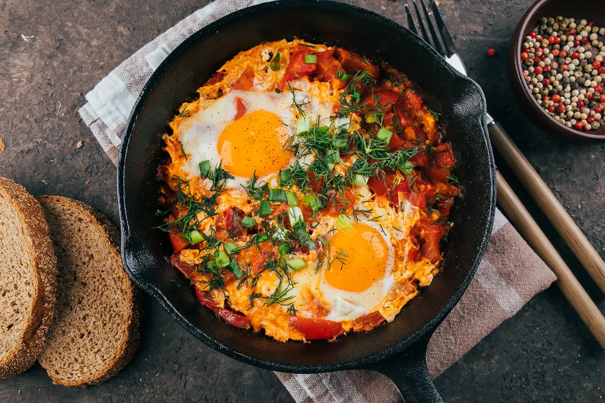 Mediterranean cousine. Shakshuka with eggs, tomato, and dill in iron pan. Top view
