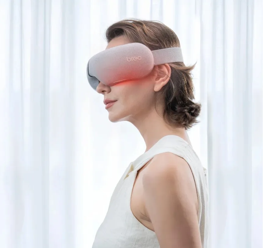 Egy nő otthon vezeték nélküli szemkörnyék- és halántékmasszírozó készüléket visel.