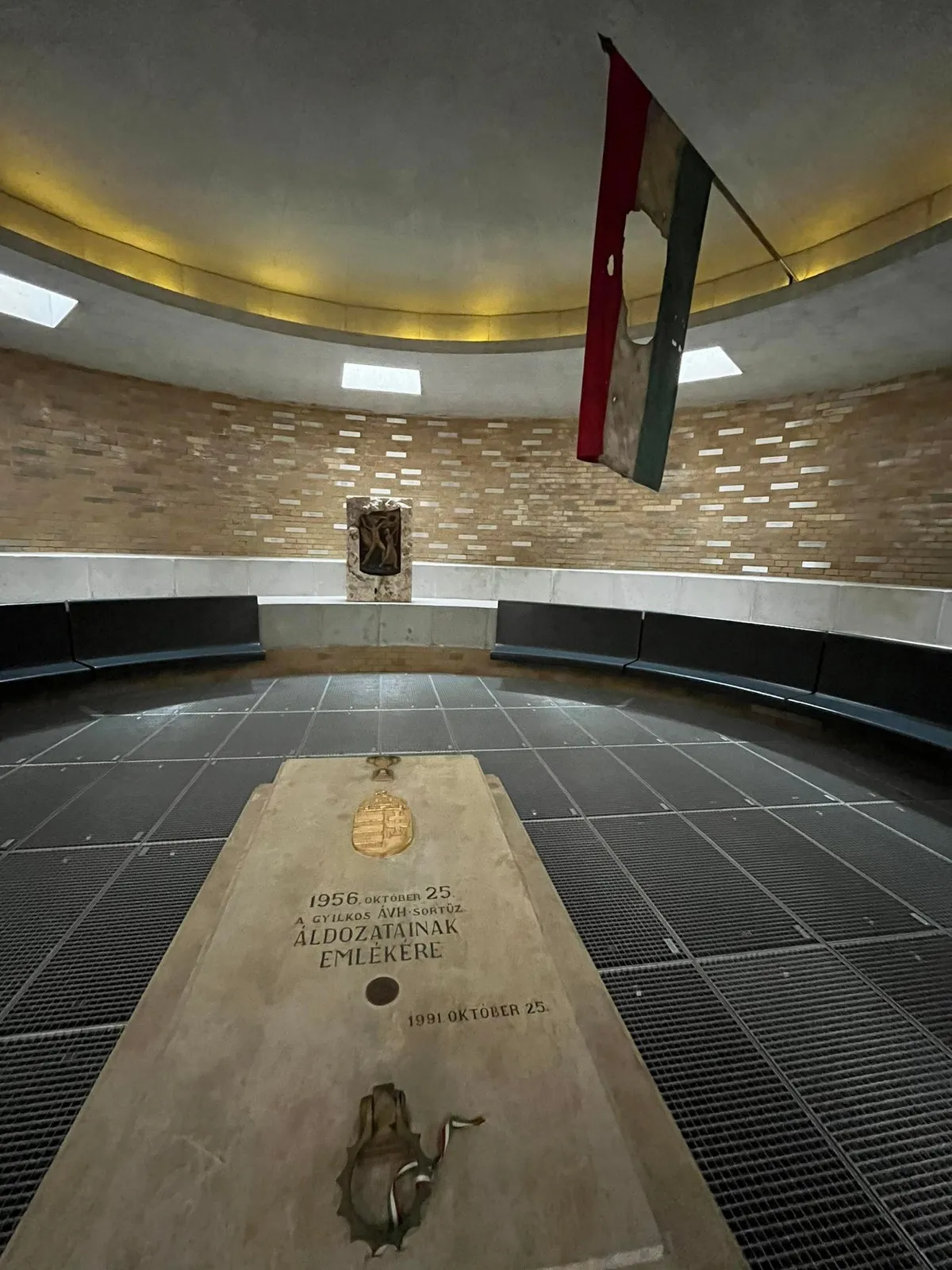 Emlékmű és lyukas közepő magyar nemzeti zászló az 1956. október 25-i harcokban elesettek emlékére