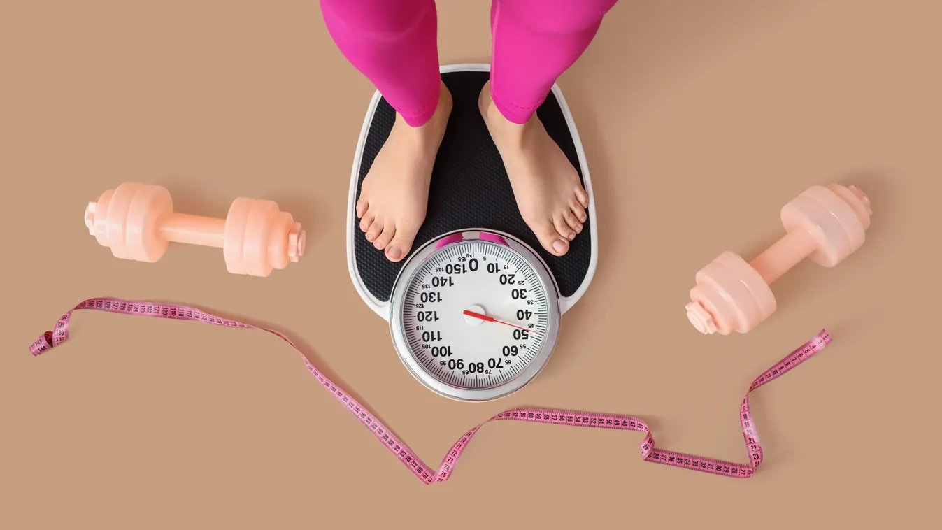Fogyókúrás tévhitekkel tisztában lévő nő mérlegen állva két kézi súlyzó és egy szalag mellett