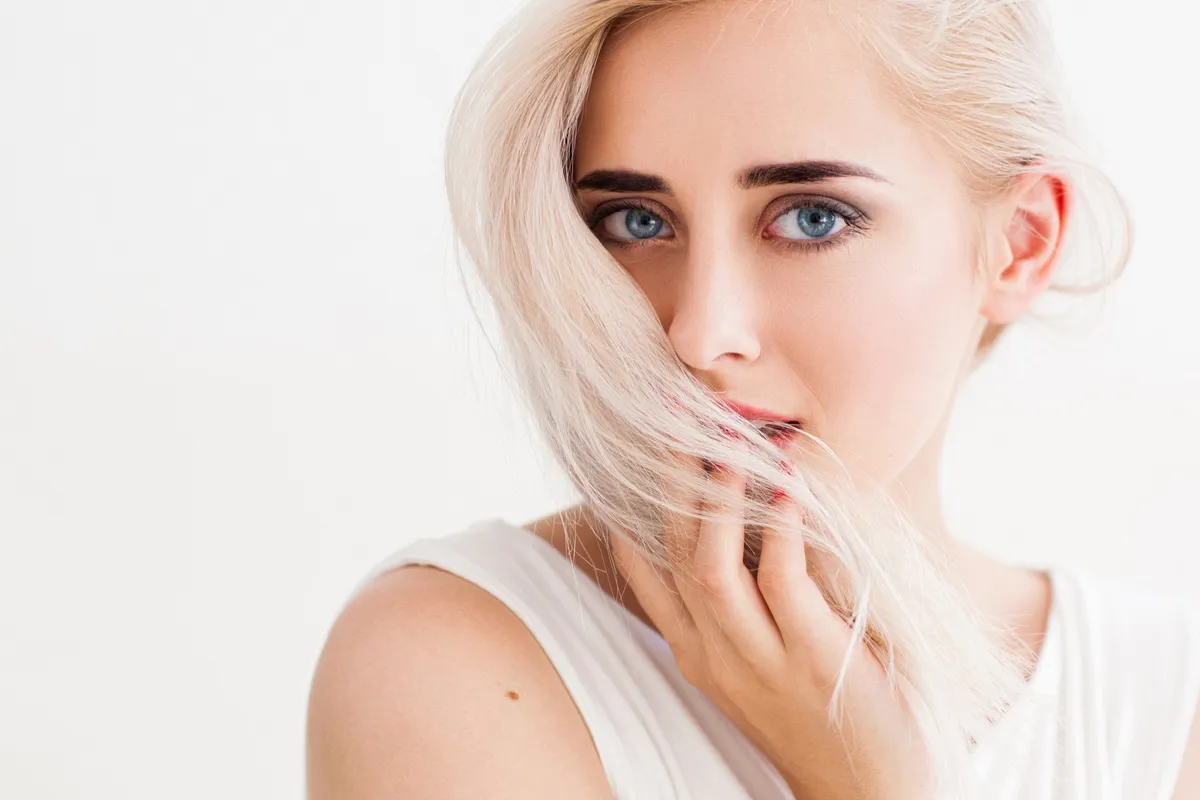 Világos hajú nő finoman megérinti a haját