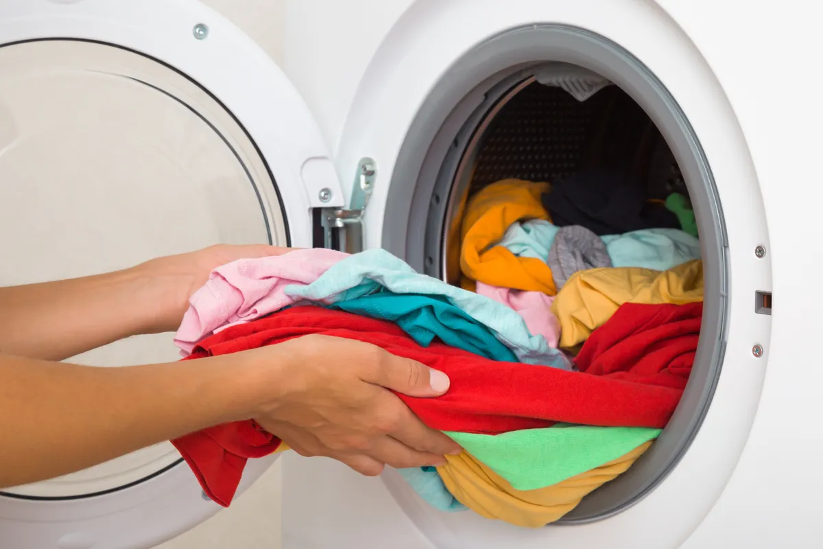 Pamutruhák mosása után egy fiatal nő színes pólókat pakol ki a mosógépből.