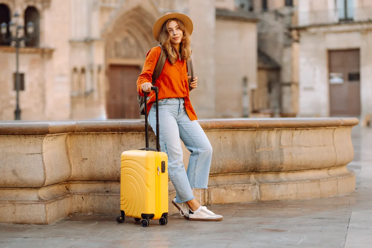 Utazós kapszulagardróbbal utazó fiatal nő egy sárga bőrönddel.