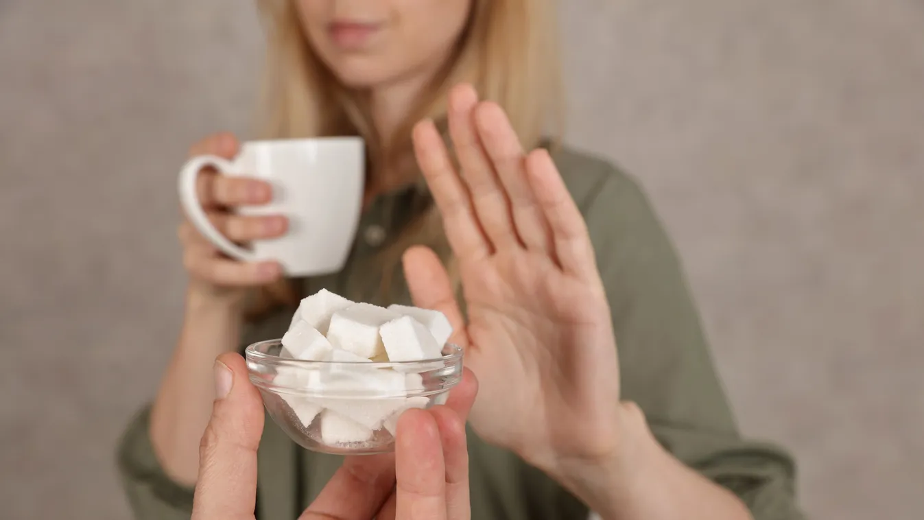 Bögre kávéval a kezében kockacukrot elutasító fiatal szőke nő, akinek fontos a cukorfogyasztás csökkentése