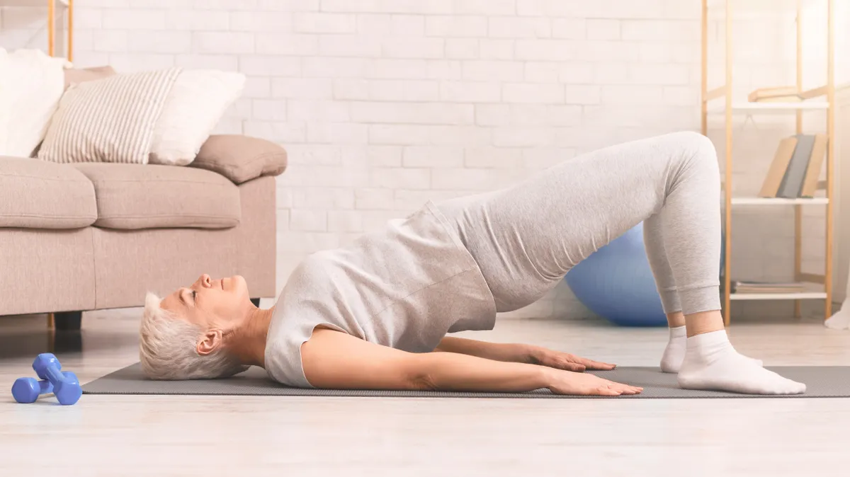 Csípőemelést végző idős nő, aki beiktatta az otthoni edzést.