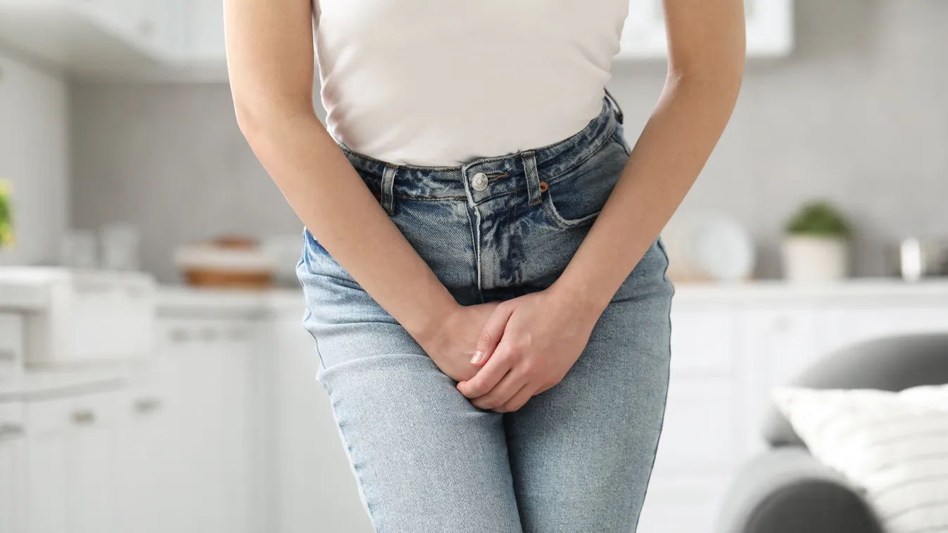 Nadrágján keresztül az intim területéhez két kézzel nyúló fiatal nő, aki a konyhában állva tudja, milyen jó a szódabikarbóna felfázásra