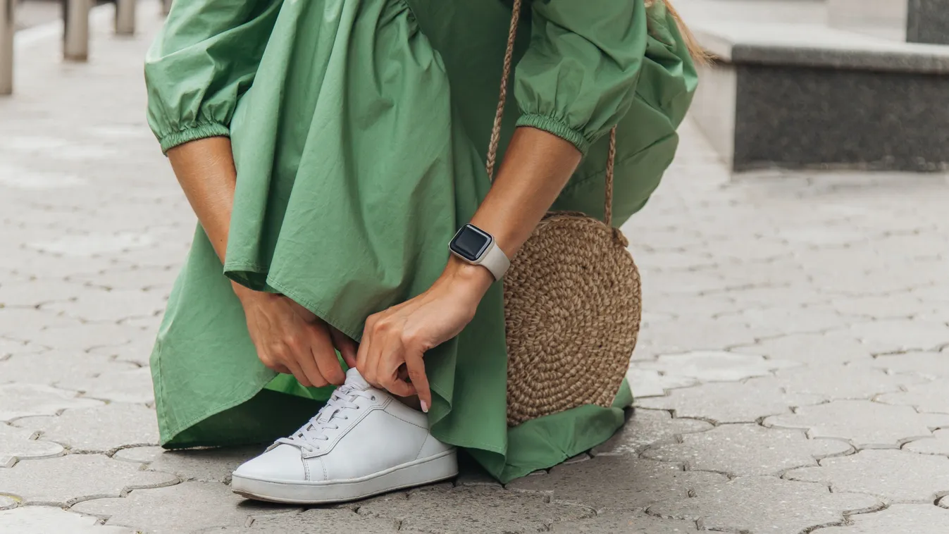 Elegáns zöld ruhás nő divatos fehér szatén sportcipőben az utcán