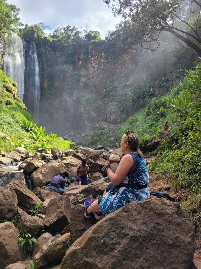 Benyo Rita egy kenyai vízesés közelében üldögél egy sziklán.