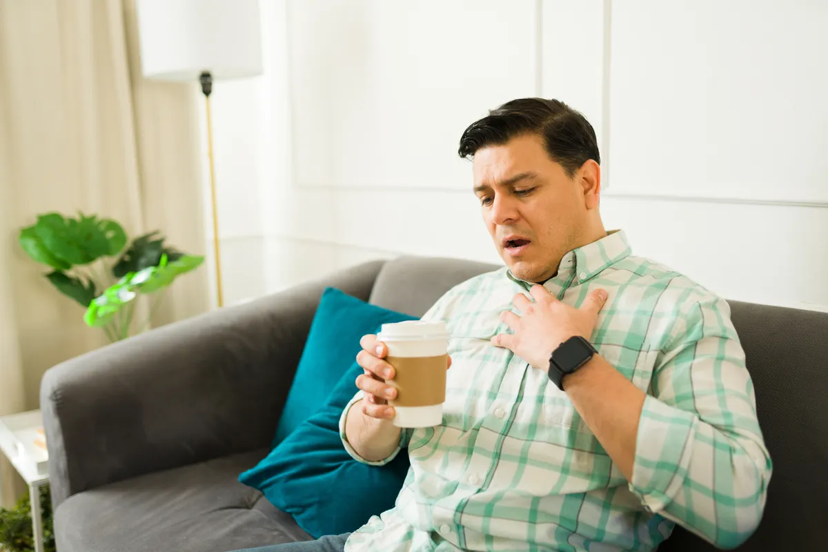 Koffeinmérgezés miatt nehézlégzéssel és légszomjjal küzdő férfi egy kanapén ülve, kávéspohárral a kezében