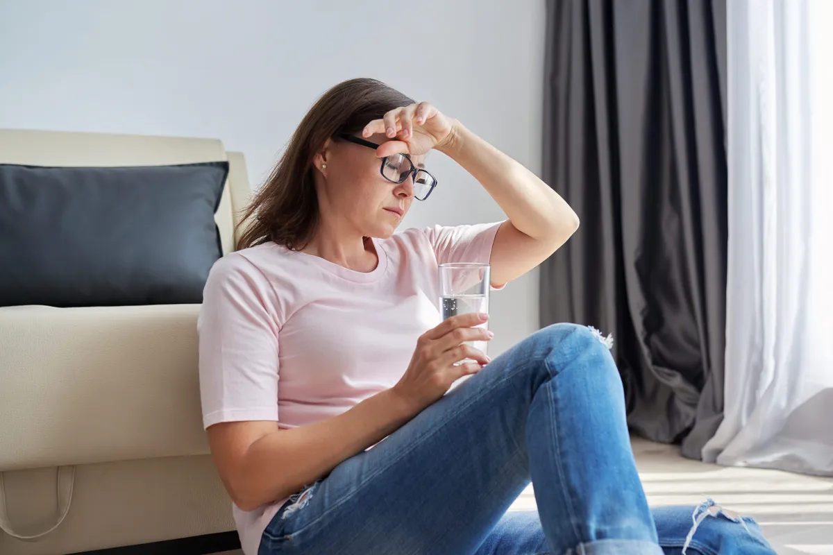 Szorongás ellen küzdő szemüveges nő ül a földön.