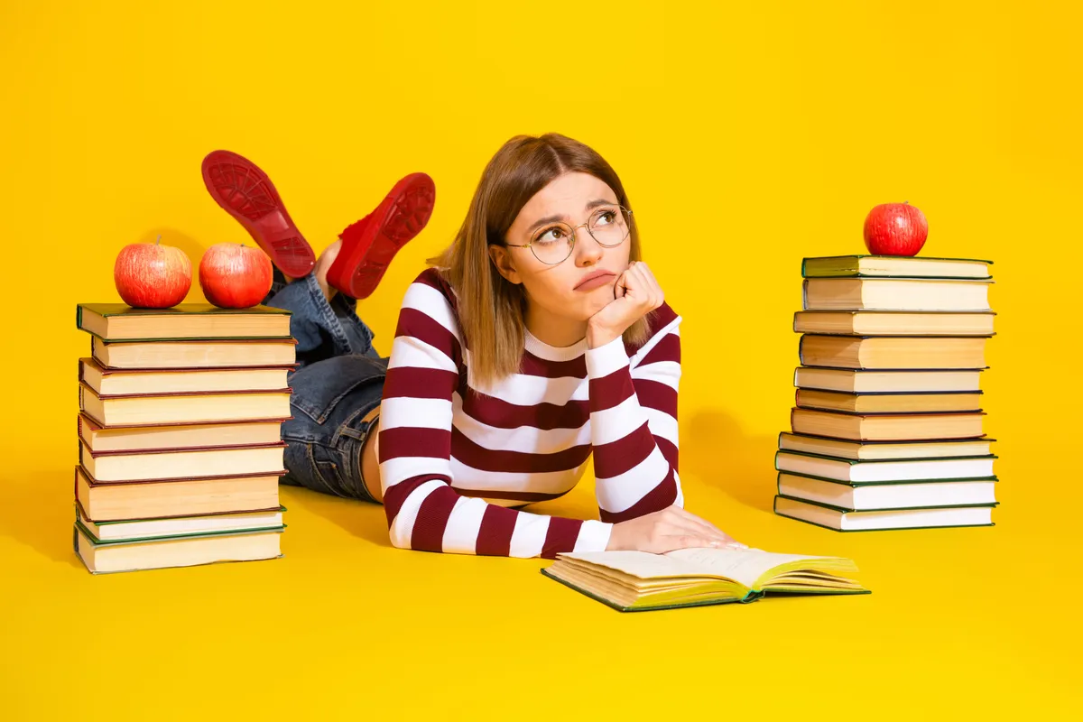 Könyvek mellett fekvő lány, aki gondolozik a helyesírási kvízen.