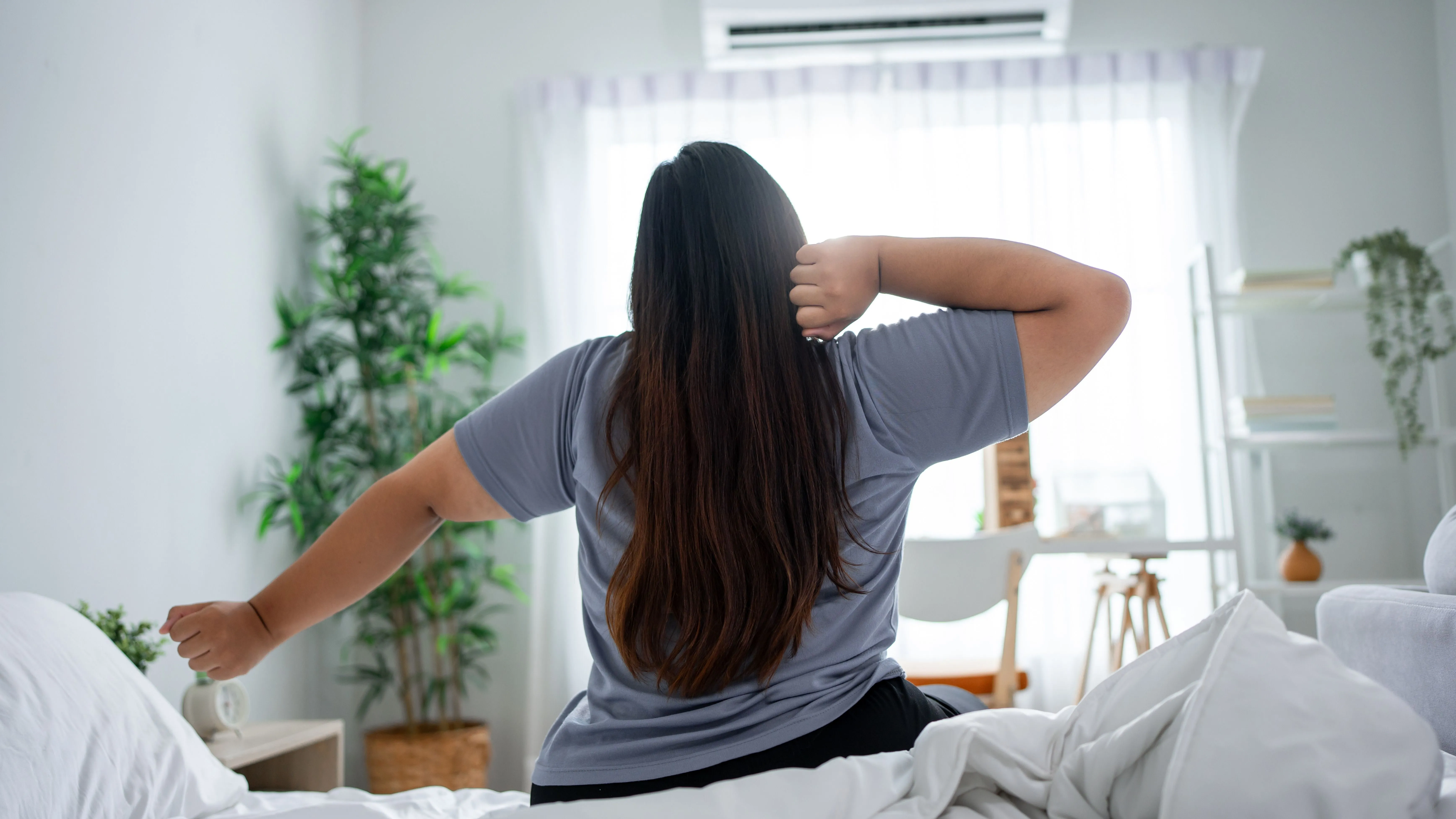 Reggeli rutin részeként időben ébredő fiatal nő az ágyán ülve reggel