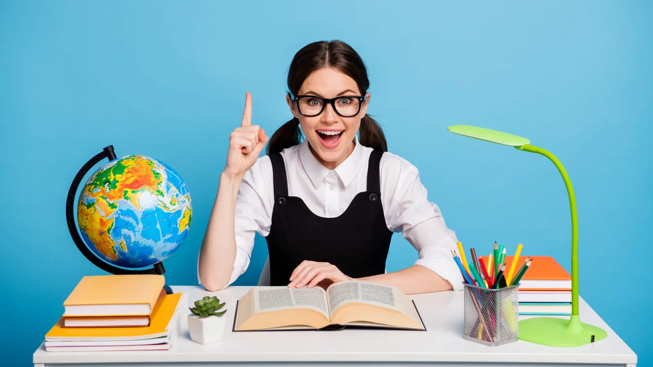 Az íróasztalnál ülő szemüveges lány a földrajzi kvízben.