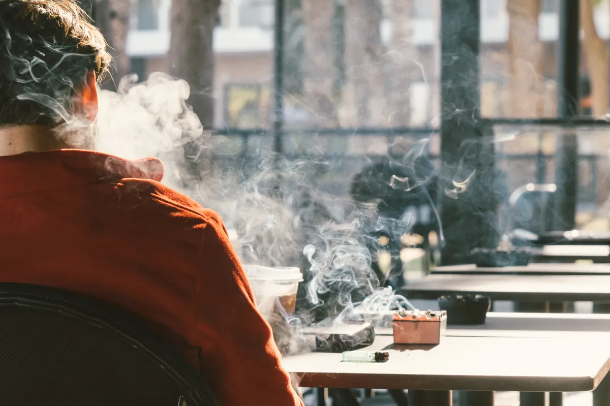 Egy férfi háttal ül és dohányzik, a dohányzás káros hatásai ott vannak a füstben.