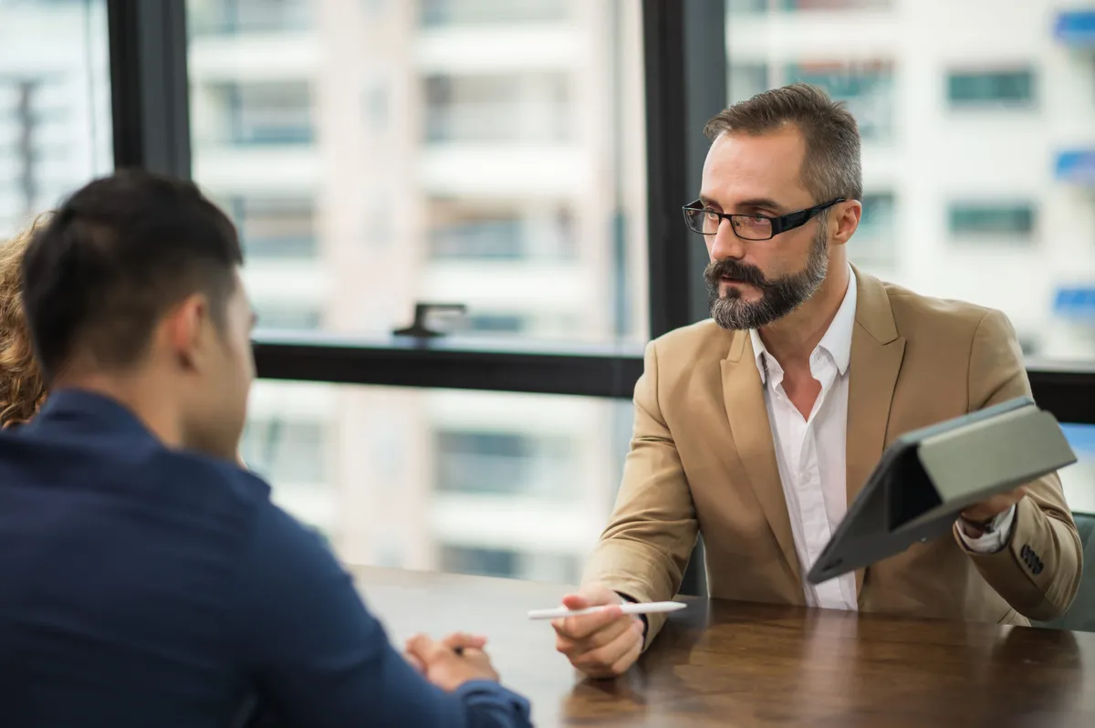 Horoszkópban szereplő kép egy munkahelyi megbeszélésről, amelyen táblagépen prezentál valamit a főnök