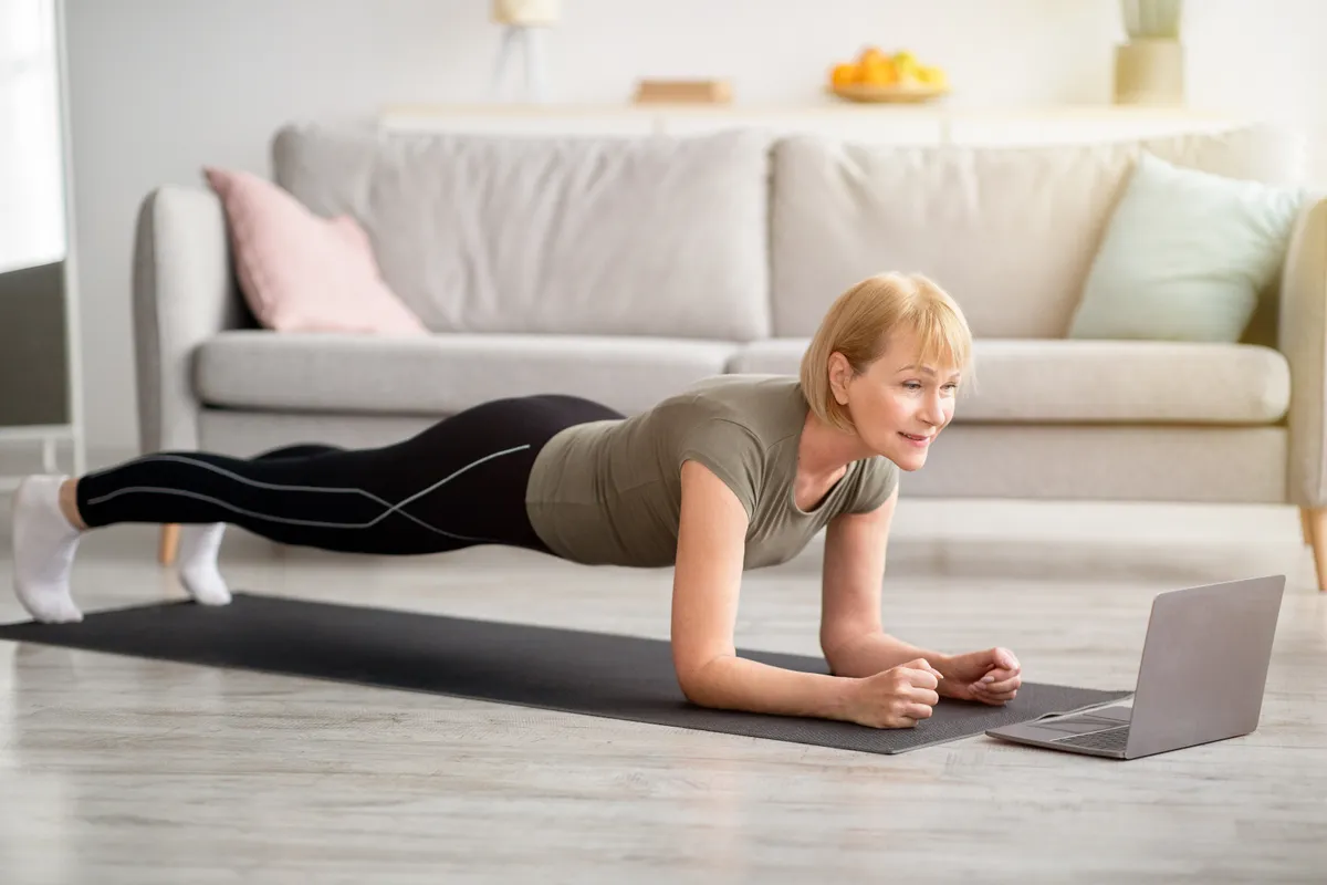 Otthoni edzést végző középkorú nő plankkel.
