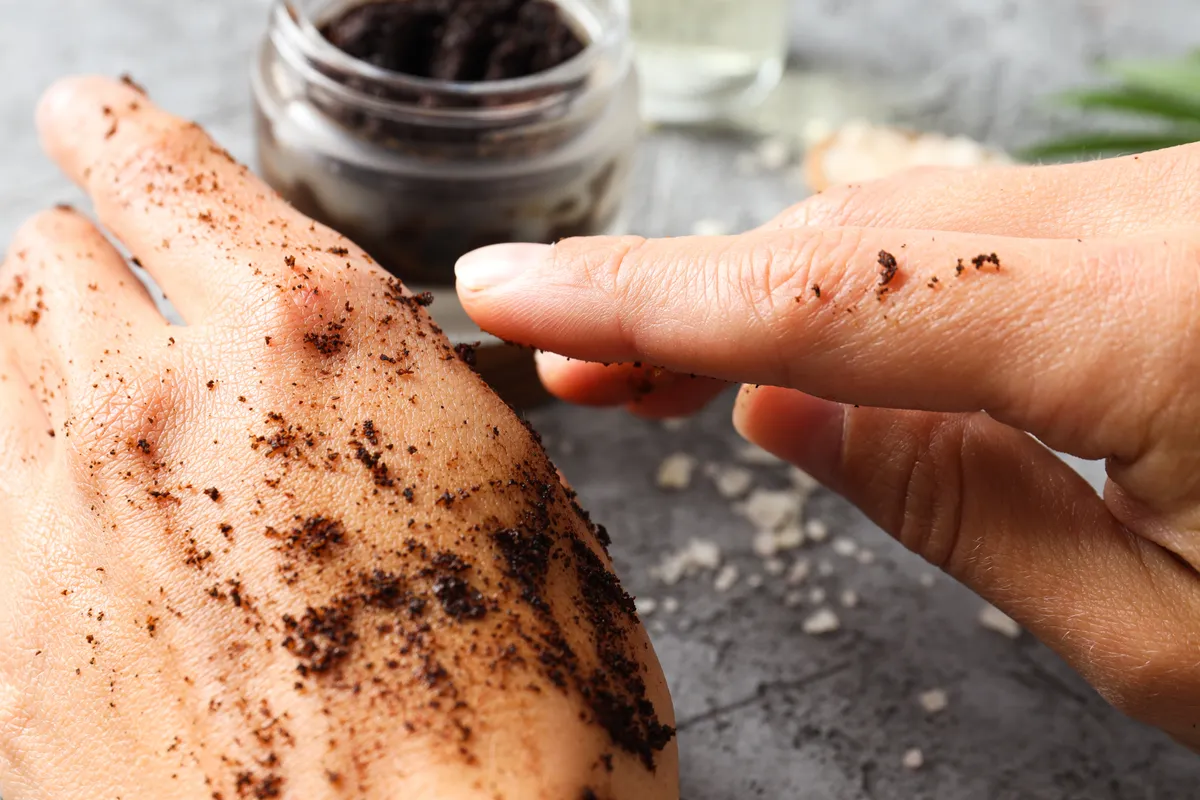 Kávé a szépségápolásban: őrölt kávéval a kézfejét kenő nő