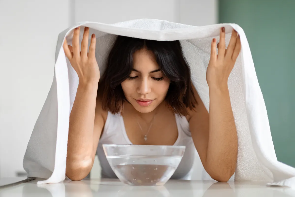 Az arcát gőzölő nő a mitesszerek elleni pakolás felvitele előtt.