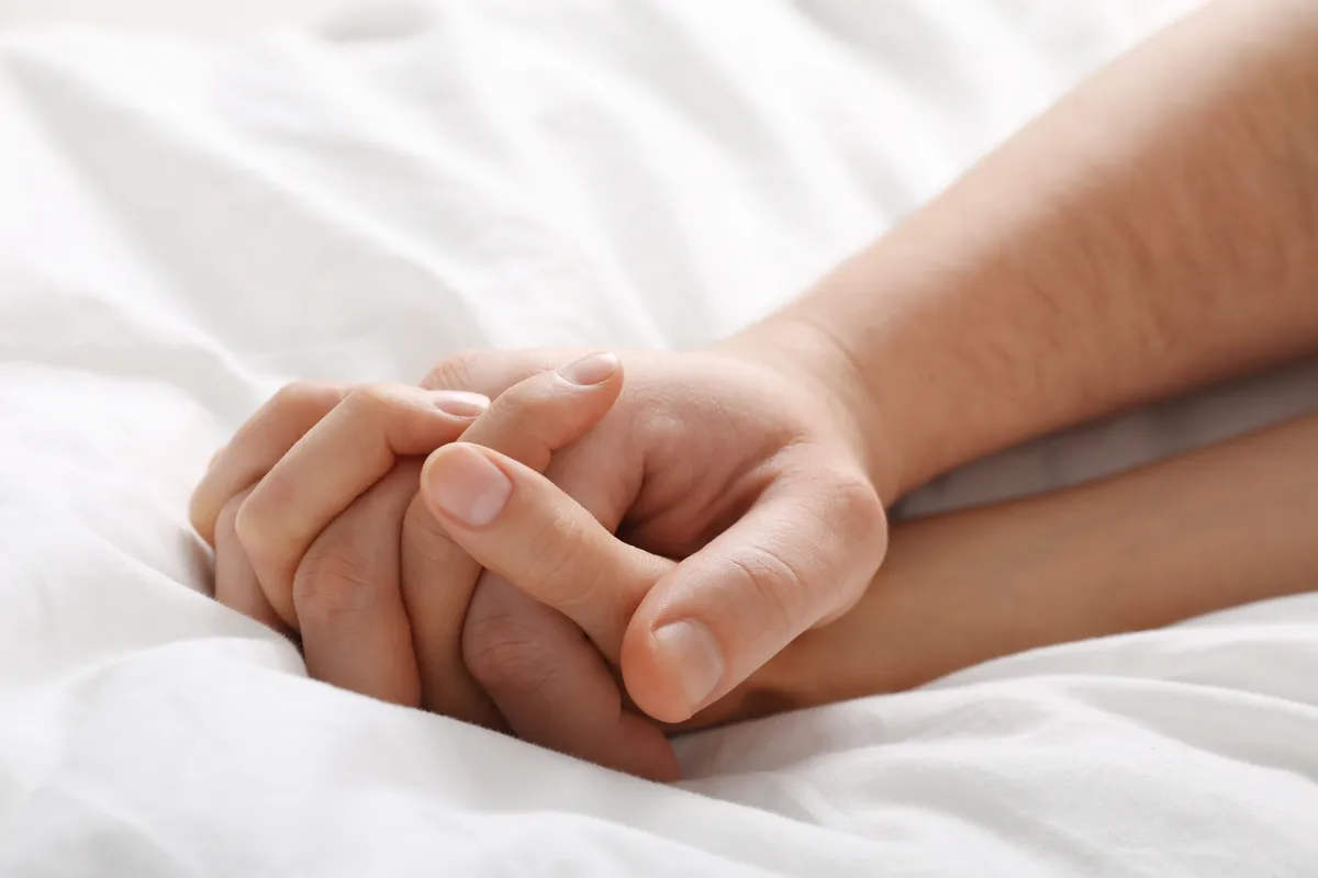 Együttlét közben egymás kezét fogó pár.