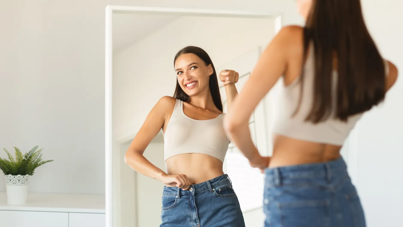 Fiatal nő nézegeti magát a tükörben, márt látszik az edzés eredménye.