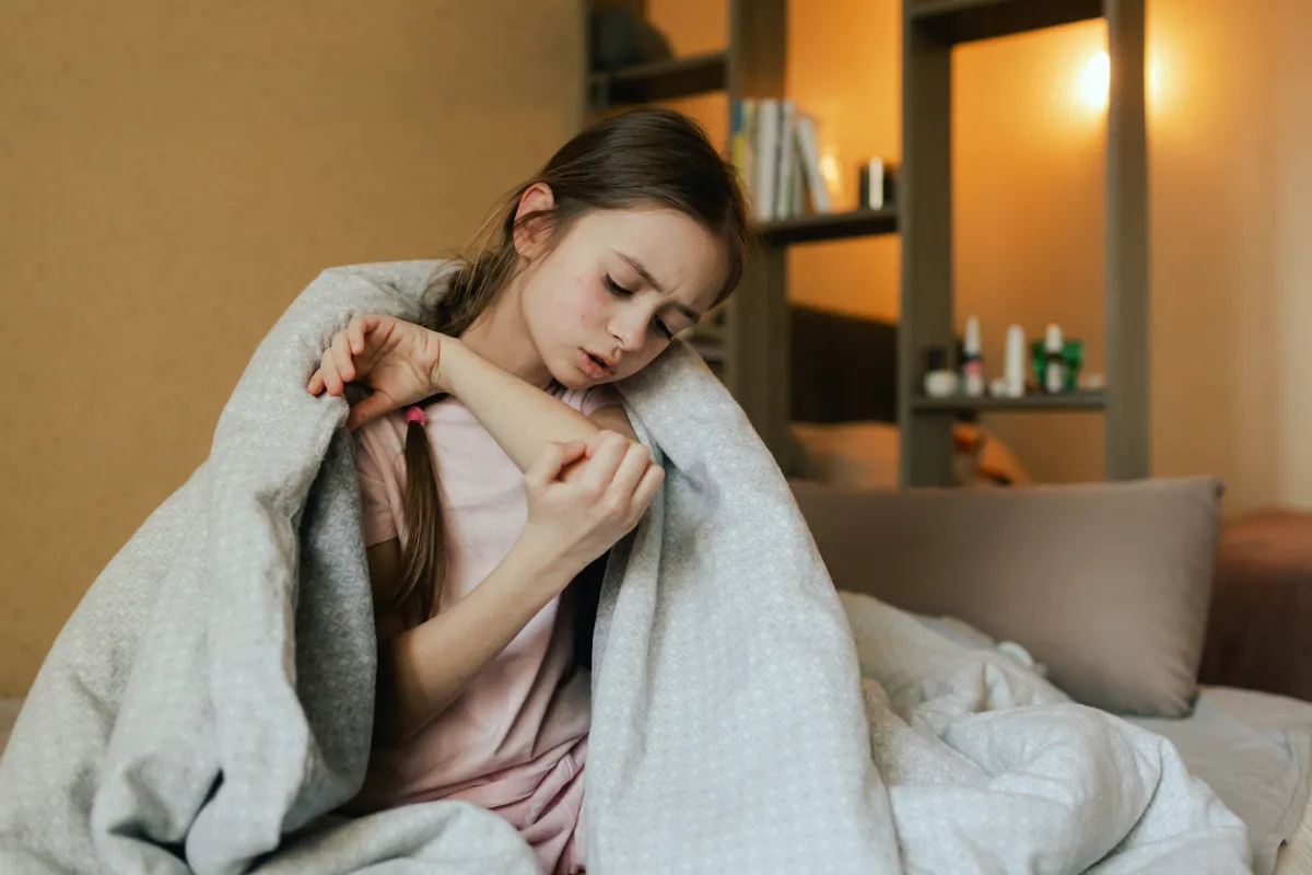 Skarlátos kislány a karján jelentkező tüneteket nézegetve az ágyon