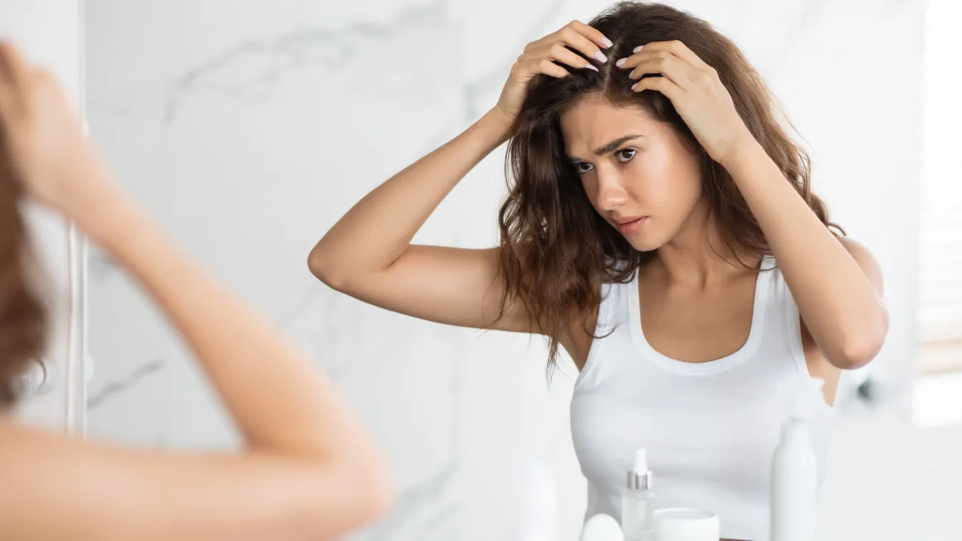 Korpa elleni fejbőrápoláson gondolkodó nő a haját vizsgálva egy tükör előtt