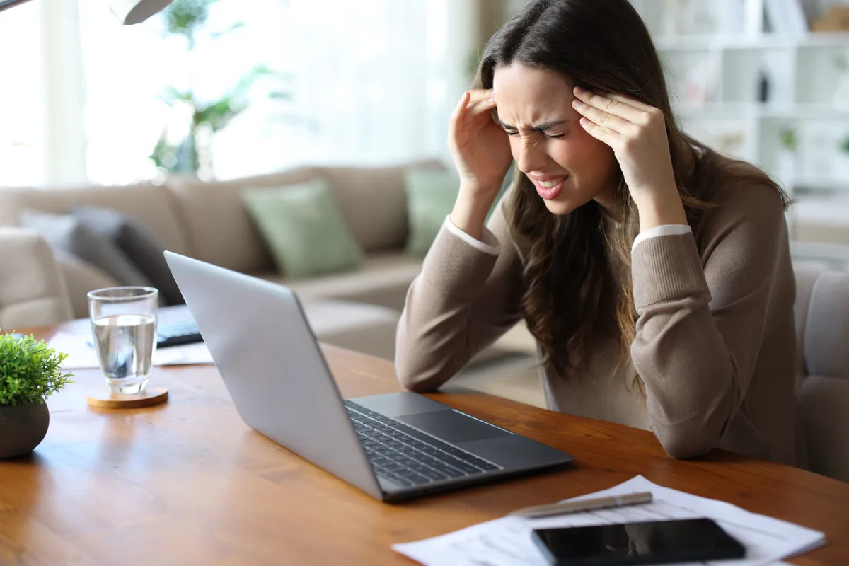 Front miatti fejfájással küzdő nő munkavégzés közben a laptopja előtt