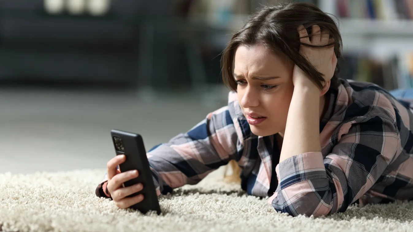 Szomorkodva nézi a telefonját egy nő a horoszkópban.