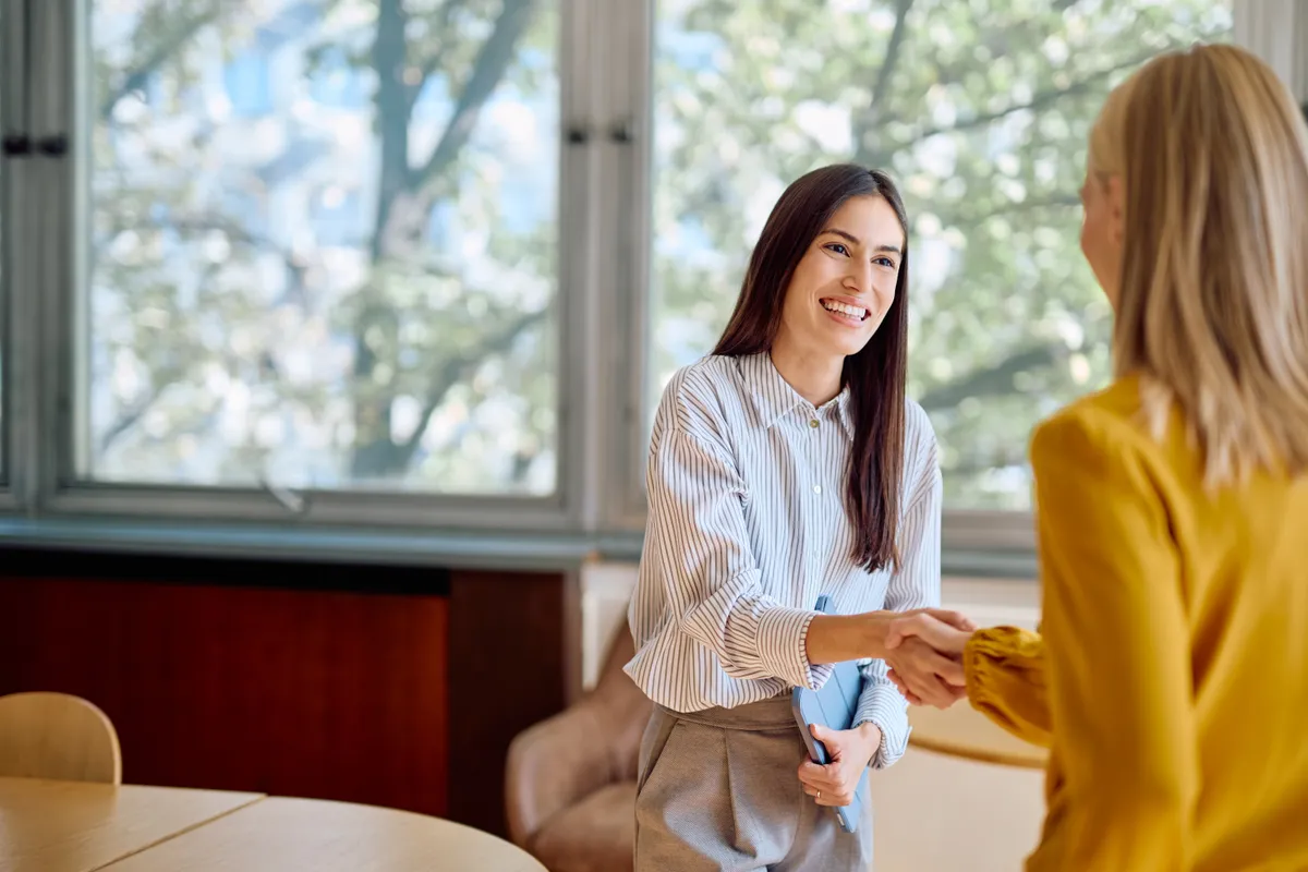 Két nő kezet fog egy irodában.
