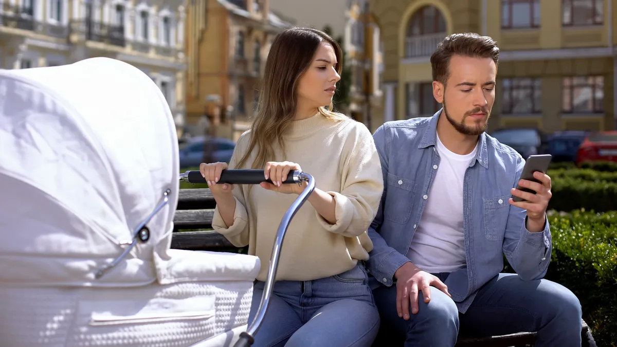 Fiatal anyuka babakocsival és a férje, aki a szeretőjével beszélget.