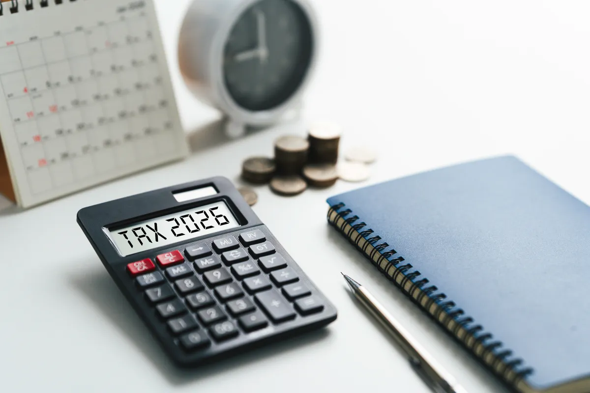 Adóbevallás 2026: asztalon számológép, füzet, toll, aprópénz, egy kis óra és naptár.