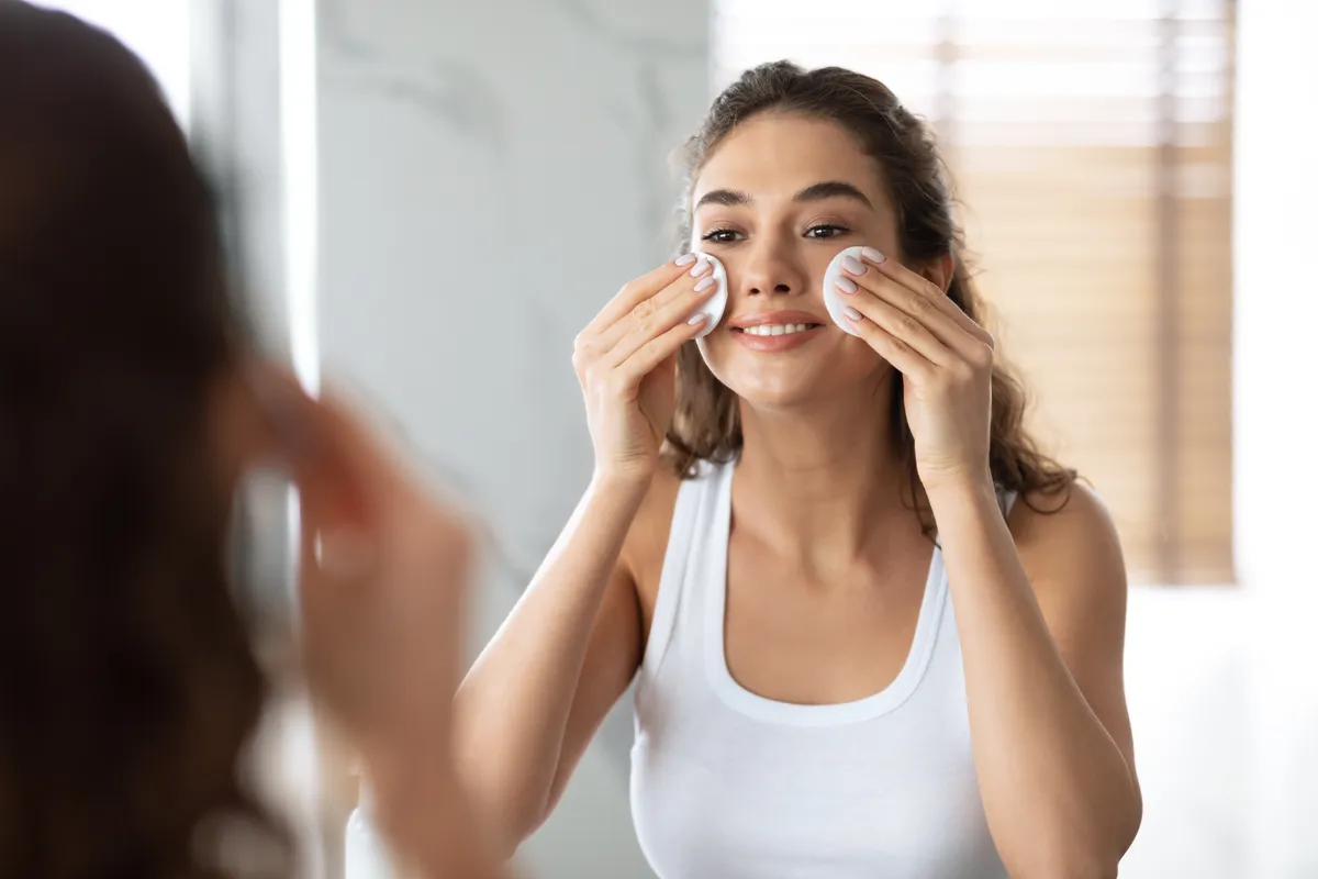 Tavaszi bőrmegújítást végző fiatal nő a tükörben az orcáihoz vattapamacsokat nyomva